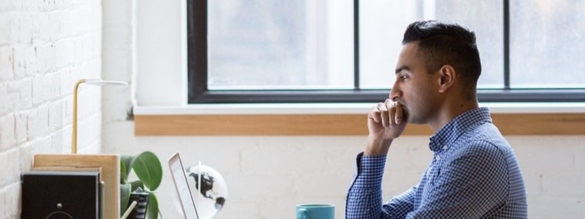 Auf dem Bild ist ein Mann am Schreibtisch zu sehen, der am Laptop arbeitet