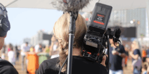 Auf dem Bild ist eine Frau mit einer Filmkamera auf der Schulter von hinten zu sehen